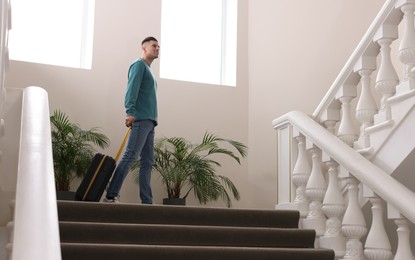 Handsome man with suitcase going up stairs in hotel
