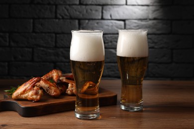 Photo of Glasses with beer and delicious baked chicken wings on wooden table