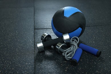 Blue medicine ball, dumbbells and skipping rope on floor, space for text