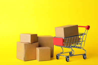 Shopping cart and boxes on yellow background. Logistics and wholesale concept