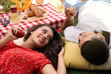 Happy couple with tasty snacks imitating picnic at home
