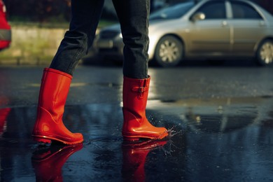 Woman with red rubber boots walking in puddle, closeup. Rainy weather