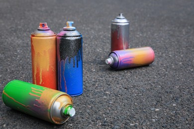 Photo of Used cans of spray paint on asphalt road. Graffiti supplies