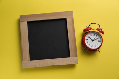 Blank chalkboard with alarm clock on yellow background, flat lay. Space for text