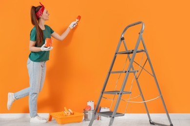 Photo of Happy designer painting orange wall with brush indoors