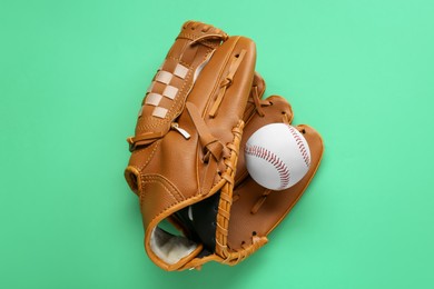 Photo of Catcher's mitt and baseball ball on green background, top view. Sports game