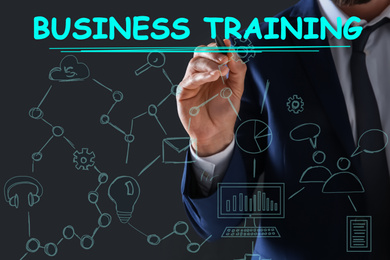 Man pointing at virtual screen with inscription BUSINESS TRAINING on dark background, closeup 
