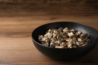 Bowl of gold nuggets on wooden table, closeup. Space for text