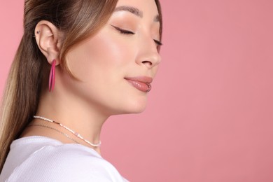 Young woman with lip and ear piercings on pink background, closeup. Space for text