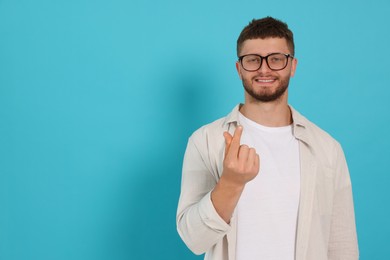 Young man showing heart gesture on light blue background, space for text