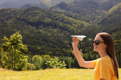 Woman throwing paper plane in mountains on sunny day. Space for text