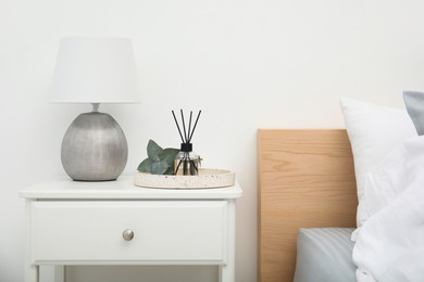Reed diffuser with lamp and eucalyptus on nightstand in bedroom
