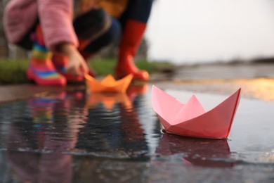 Little girl and her mother playing near puddle outdoors, focus on paper boat