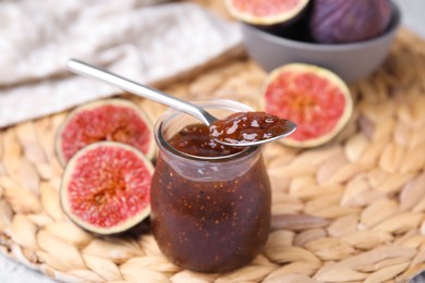 Glass jar of tasty sweet fig jam with spoon and fruits on table
