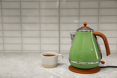 Modern electric kettle and cup of tea on grey marble kitchen counter. Space for text