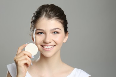 Beautiful girl with foundation smear on her face holding sponge against grey background