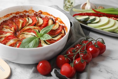 Photo of Delicious ratatouille and ingredients on white marble table, closeup