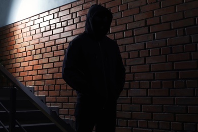 Photo of Silhouette of mysterious man in hoodie indoors. Dangerous criminal