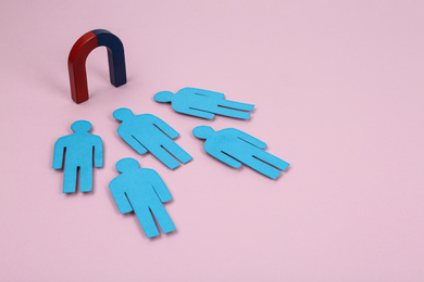 Magnet attracting paper people on pink background