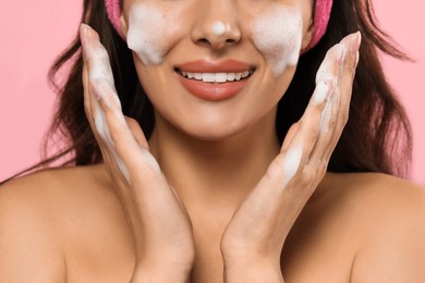 Beautiful woman applying facial cleansing foam on pink background, closeup