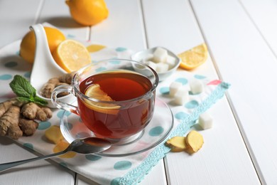 Photo of Cup of delicious ginger tea, sugar cubes and lemons on white wooden table