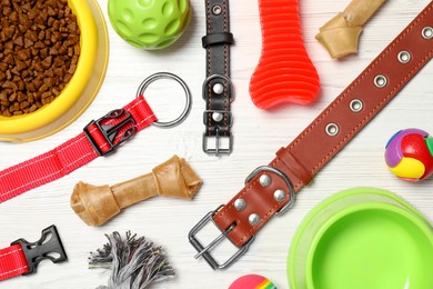 Flat lay composition with dog collars, toys and food on white wooden table