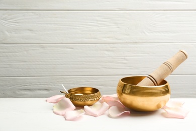 Composition with golden singing bowl and petals on white wooden table, space for text. Sound healing