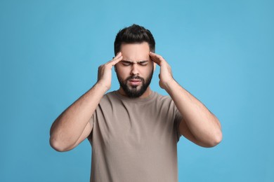 Young man suffering from headache on light blue background
