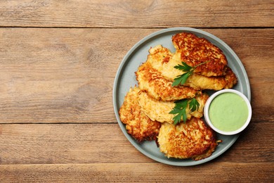 Photo of Tasty parsnip cutlets with parsley and sauce on wooden table, top view. Space for text
