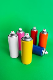 Colorful cans of spray paints on green background