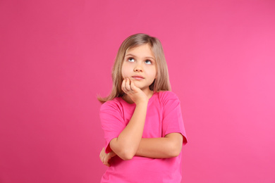 Thoughtful little girl wearing casual outfit on pink background
