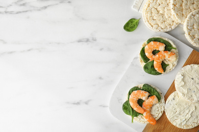 Puffed rice cakes with shrimps and basil on white marble table, flat lay. Space for text