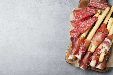 Photo of Tasty prosciutto and salami on light grey table, top view. Space for text