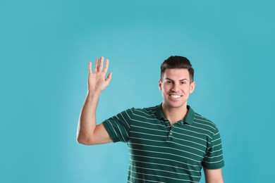 Photo of Cheerful man waving to say hello on turquoise  background