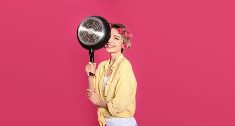 Young housewife with frying pan on pink background