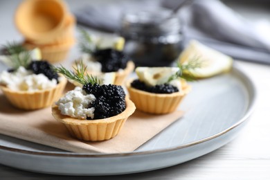 Photo of Delicious tartlets with black caviar, cream cheese and lemon served on light table, closeup