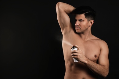 Handsome man applying deodorant to armpit on black background, space for text