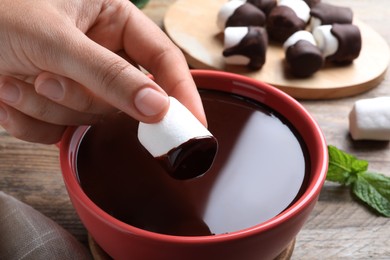 Woman dipping marshmallow into melted chocolate at wooden table, closeup