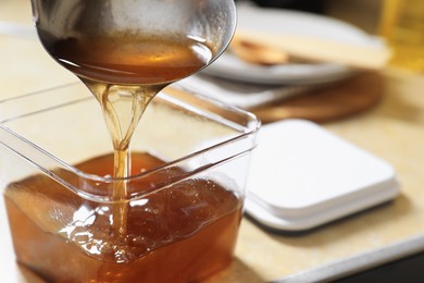Pouring used cooking oil with ladle into container on beige table in kitchen, closeup