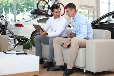 Young salesman working with client in modern car dealership