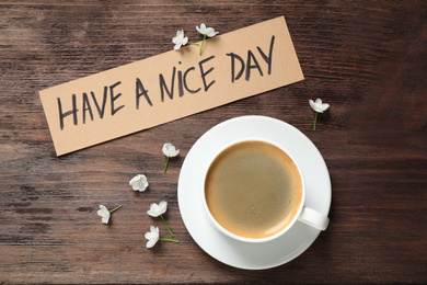 Delicious morning coffee, flowers and card with HAVE A NICE DAY wish on wooden table, flat lay