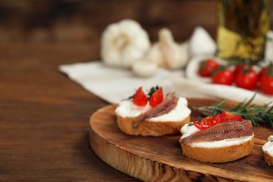 Photo of Delicious sandwiches with cream cheese, anchovies and tomatoes on wooden table, space for text