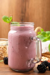 Delicious blackberry smoothie in mason jar and berries on wooden table