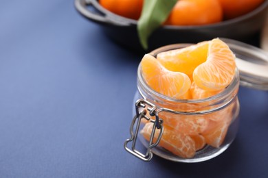 Photo of Glass jar of fresh juicy tangerine segments on blue table, space for text