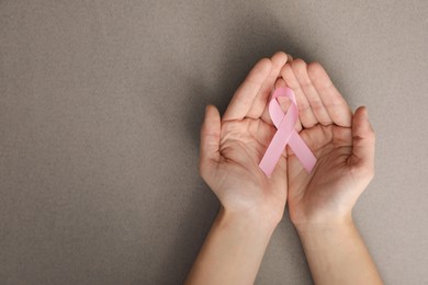 Woman holding pink ribbon on grey background, top view with space for text. Breast cancer awareness concept