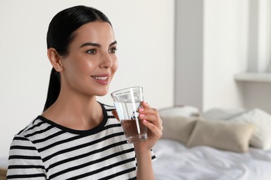 Young woman with glass of water indoors, space for text. Refreshing drink