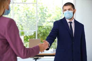 Man and woman in protective face masks shaking hands to say hello in office, closeup