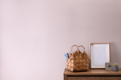 Wooden chest of drawers with stylish bag, decor and empty frame near light wall in room, space for text. Interior design
