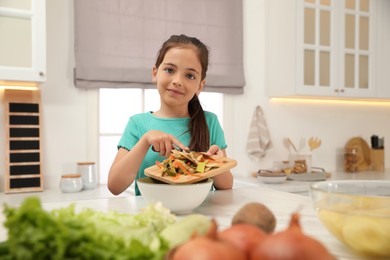 Little girl with cutting board and knife scraping  vegetable peels into bowl in kitchen