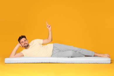 Man on soft mattress pointing upwards against orange background